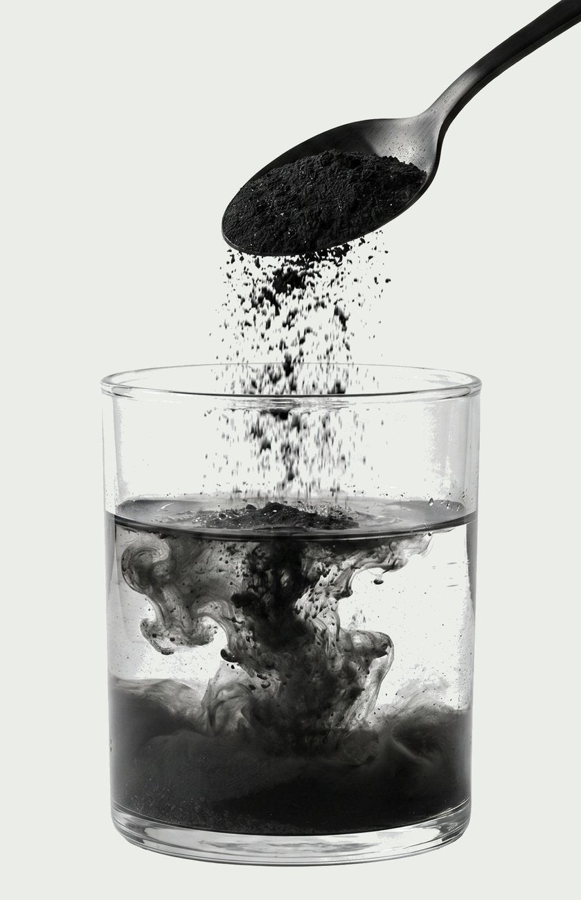 A spoonful of activated charcoal powder poured into a glass of water, turning it black
